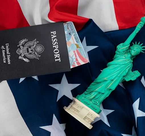 A U.S. passport lies on an American flag, accompanied by a small Statue of Liberty figurine, symbolizing patriotism and travel.