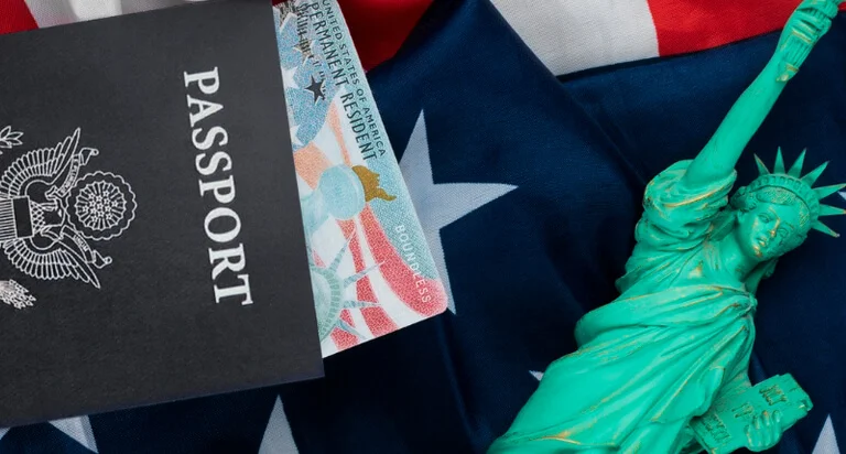 A U.S. passport lies on an American flag, accompanied by a small Statue of Liberty figurine, symbolizing patriotism and travel.