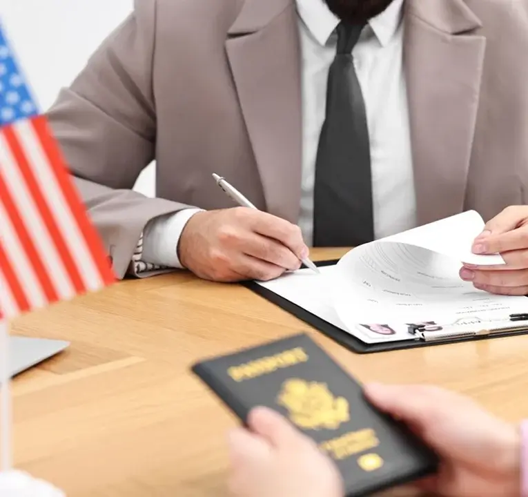 Person handing over a U.S. passport and documents to an immigration officer at a desk.