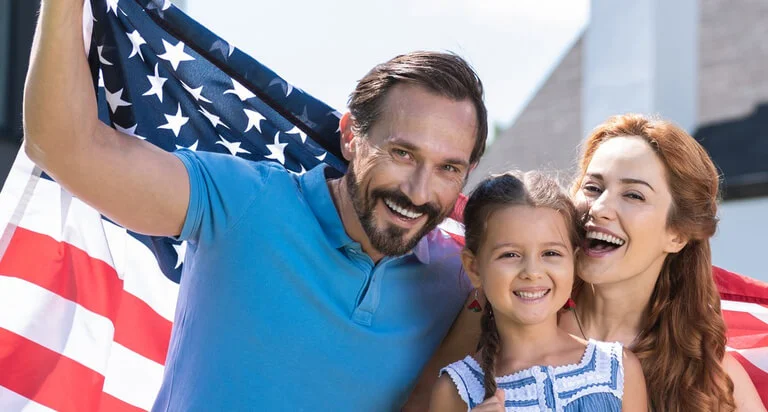 A family proudly holds an American flag outside their modern home, celebrating together in a joyful and patriotic moment.