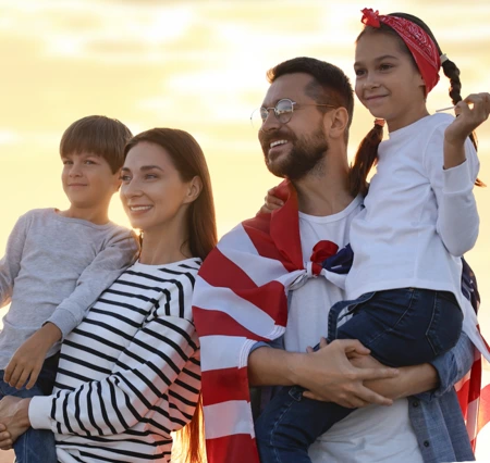 Joyful family with an American flag, enjoying a sunset together, creating a warm and patriotic atmosphere.